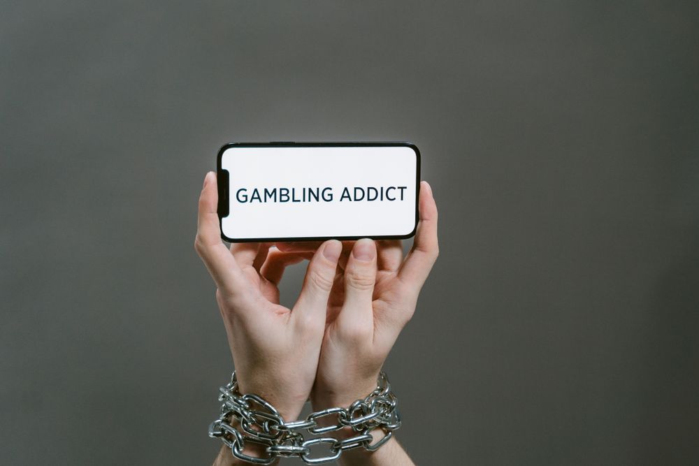 Tangan terikat memegang telepon dengan teks gambling addict